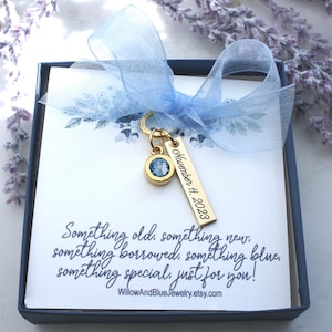 Op de afbeelding: Een geschenkdoos met een lichtblauw lint en een gouden bedel. De bedel heeft een blauwe edelsteen en een label met de tekst "November 11, 2023". De doos bevat een kaart met de tekst "Something old, something new..." en de Etsy shopnaam.