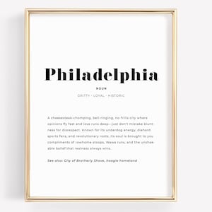 Może przedstawiać: Oprawiony wydruk ze złotą obwódką zawiera słowo "Philadelphia" pogrubioną czcionką. Poniżej tekst definiuje miasto słowami takimi jak "gritty" i "historic". Wydruk zawiera opis kultury Filadelfii.
