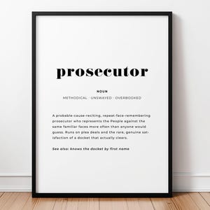 May include: A framed wall art print featuring a dictionary-style definition of the word prosecutor. The text includes the noun label, adjectives methodical, unswayed, overbooked, and a paragraph describing the role, ending with see also: knows the docket by first name.