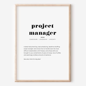 Könnte beinhalten: Ein gerahmter Druck mit der Definition von "Projektmanager" in schwarzem Text auf weißem Hintergrund. Die Definition umfasst das Nomen, Schlüsselmerkmale und eine humorvolle Beschreibung. Der Rahmen ist hellholzfarben.