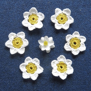 May include: Seven crocheted white flowers with yellow centers. The flowers are arranged in a circle on a blue background.
