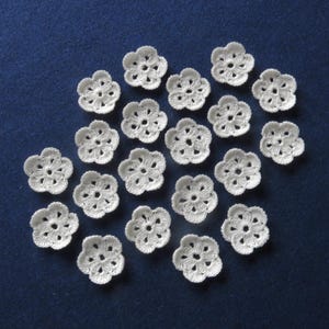 May include: A collection of 18 white crocheted flower embellishments. The flowers are delicate and intricate, with a five-petal design.