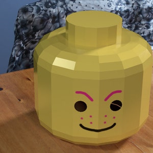 May include: A yellow Lego head costume with pink eyebrows and a smile. The head has black eyes and pink freckles.