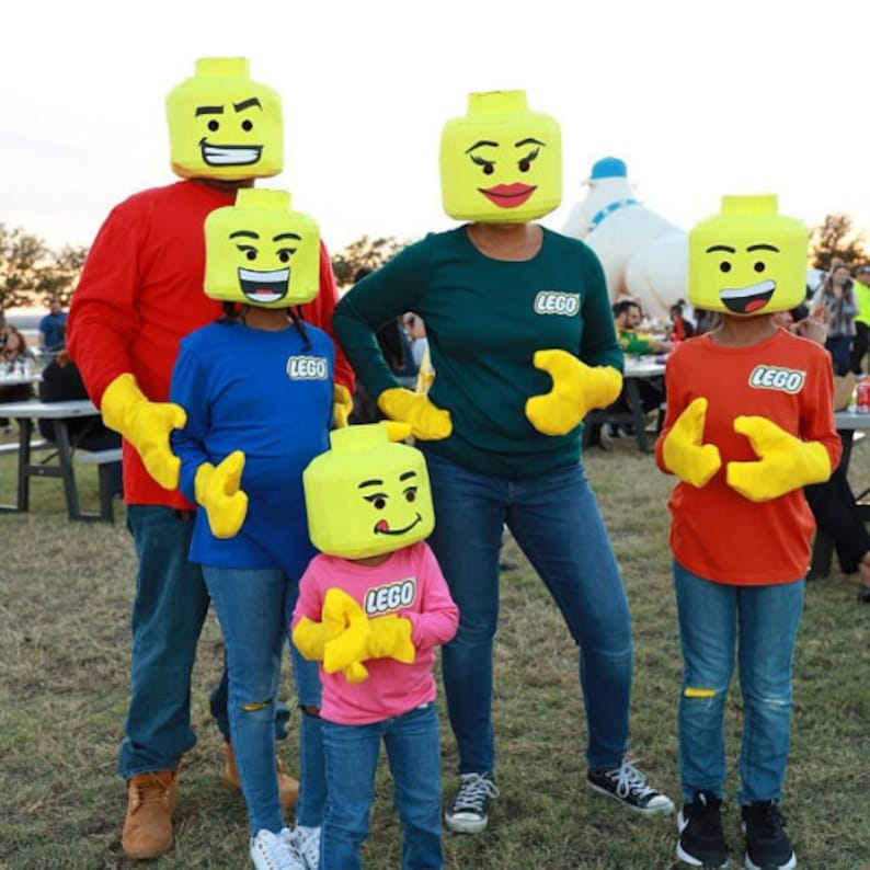 May include: A group of people dressed as LEGO minifigures. The people are wearing yellow LEGO head costumes with different facial expressions. The costumes include red, blue, green, and pink shirts. The people are standing in front of a white background.