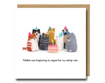 Puede incluir: Una tarjeta de felicitación cuadrada con borde marrón, que muestra un grupo de figuras de gatos de fieltro con sombreros de fiesta. Una pequeña tarta con una vela está frente a ellos. El texto dice: "Tiddles was beginning to regret her no catnip rule."