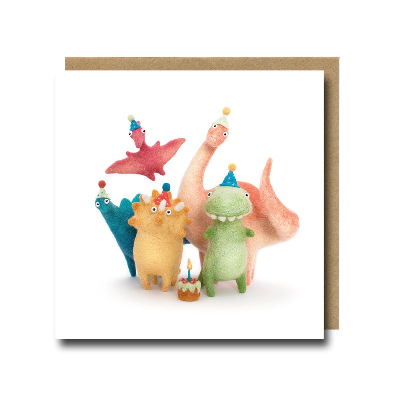 A charming birthday card with a white background featuring five needle felt dinosaurs wearing party hats. The dinosaurs are a peach diplodocus, a green tyrannosaurus rex, a blue stegosaurus, a yellow triceratops and a red pteradactyl. The dinosaurs are all smiling and looking at the viewer. There is a small birthday cake with a single candle in front of the dinosaurs.