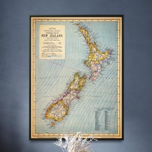 May include: A framed vintage map of New Zealand is displayed on a dark blue wall. Below, a wooden dining table is set with four places, surrounded by brown chairs. A vase with dried flowers is in the center.