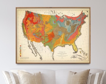 May include: A vintage map of the United States showing the geological formations of the country. The map is framed in a wooden frame and is hanging on a white wall above a white sofa with beige cushions. The sofa is in a living room setting with a wooden coffee table and a lamp.