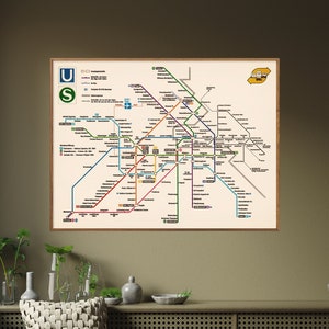 May include: A framed map of the Munich subway system with lines labeled U and S. The map is on a beige wall above a wicker bench and a cabinet with a woven rattan front.