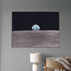 May include: A framed photograph of Earth rising over the lunar surface, as seen from the moon. The image is in a dark room with a lamp and a couch in the foreground.