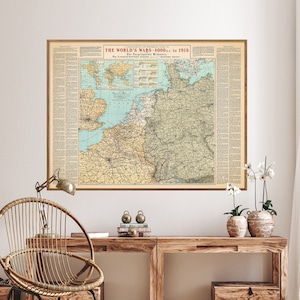 May include: A framed vintage map titled "THE WORLD'S WARS - 4000 B.C. to 1918" hangs on a white wall. The map features a detailed depiction of Europe and surrounding regions, with a light brown wooden frame. The room includes a wooden desk and a wicker chair.