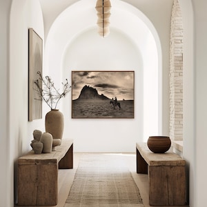 May include: An interior hallway with a neutral color palette. The space features a framed sepia-toned landscape photograph, rustic wooden benches, and a woven runner. Decorative vases and a hanging light fixture add to the aesthetic.