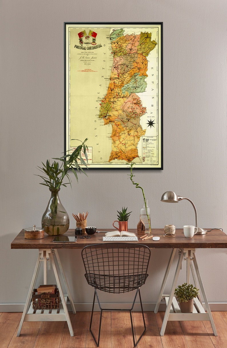 Puede incluir: Un mapa vintage de Portugal en un marco negro colgado en una pared gris claro sobre un escritorio de madera con una silla de alambre negro, un jarr&oacute;n con plantas verdes, una taza de cobre, una l&aacute;mpara y una taza blanca.