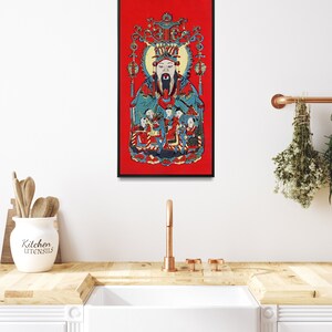 May include: A framed print of a traditional Chinese painting depicting a deity with a long beard and a crown, surrounded by smaller figures. The painting is set against a red background.