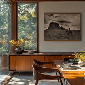 May include: A dining room with a mid-century modern aesthetic. Features include a wooden credenza, dining table, and chairs. A framed black and white photograph of a mountain landscape hangs on the wall. Large windows offer a view of the outdoors.