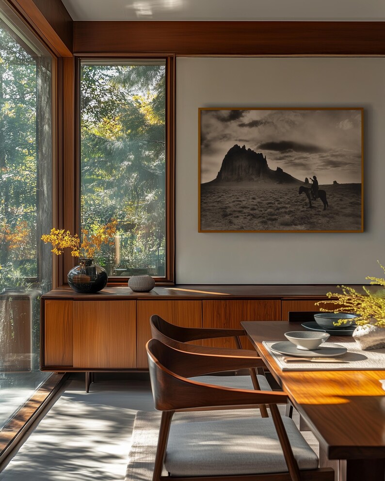 May include: A dining room with a mid-century modern aesthetic. Features include a wooden credenza, dining table, and chairs. A framed black and white photograph of a mountain landscape hangs on the wall. Large windows offer a view of the outdoors.