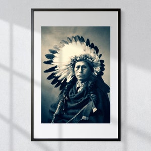May include: A black and white portrait of a Native American man wearing a traditional headdress with feathers. The man is looking directly at the camera with a serious expression.
