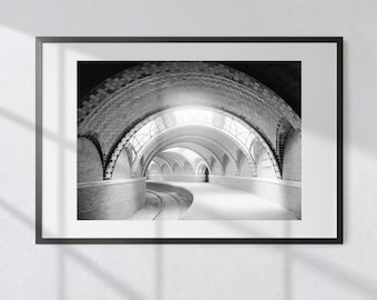 May include: Black and white framed print of a curved tunnel with arched ceilings and brickwork. The tunnel has a track running through it, and a person is visible in the distance. The print is displayed on a white wall.