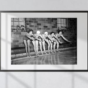 Puede incluir: Cinco mujeres en traje de baño y gorro de baño se encuentran en el borde de una piscina, preparándose para zambullirse. Están alineadas en una fila, con los brazos extendidos y los cuerpos inclinados hacia adelante. La piscina está vacía y el fondo es una pared de ladrillo.