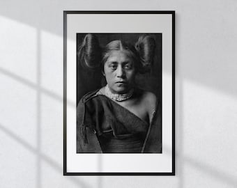 May include: Black and white portrait photograph of a Native American woman wearing a beaded necklace and a dark shawl. Her hair is styled in two buns on top of her head.