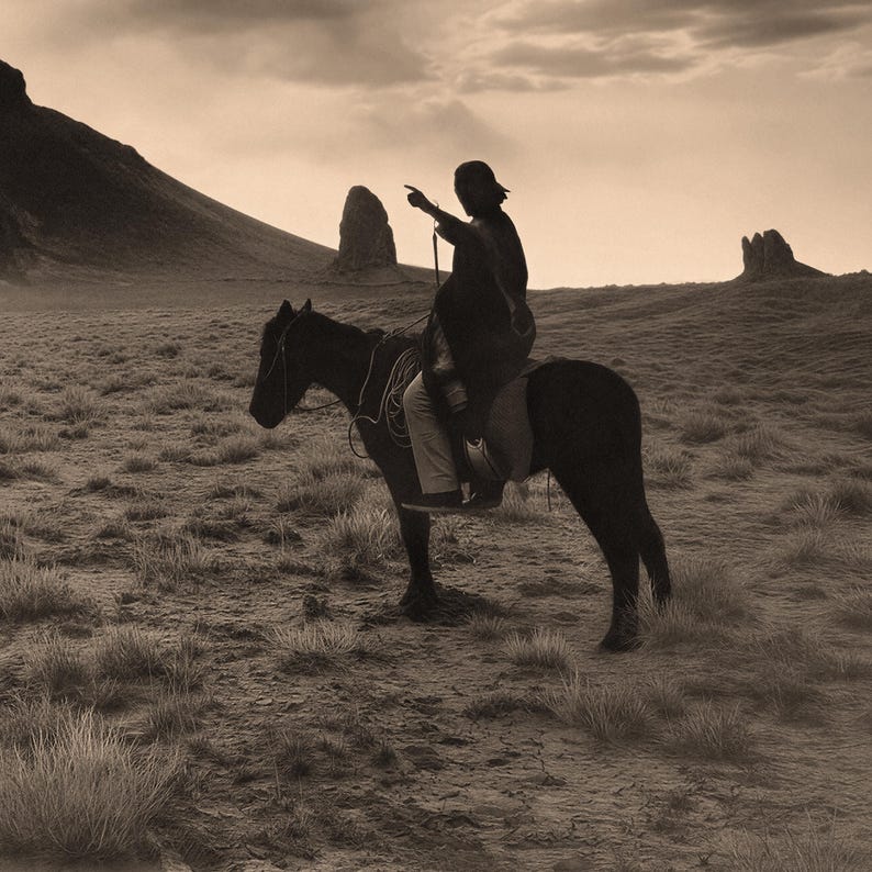 May include: Sepia-toned image of a person riding a horse across a grassy plain. The rider, silhouetted against the sky, points towards the horizon. The horse is saddled and bridled, and the landscape includes distant rock formations and a cloudy sky.