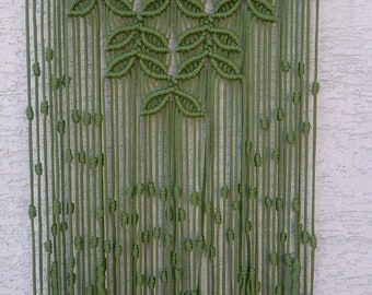 May include: A green macrame wall hanging with a leaf pattern. The hanging is made with thick cotton cord and has a wooden dowel at the top.