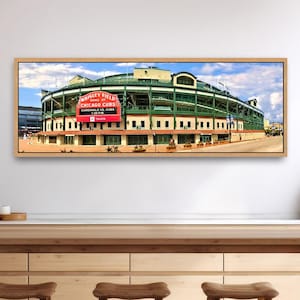 May include: A panoramic wall art print featuring the exterior of Wrigley Field, home of the Chicago Cubs. The stadium displays a prominent red marquee sign with white text against a green structure under a bright blue sky with clouds.