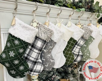 May include: A collection of Christmas stockings with various patterns, including snowflakes, plaid, and deer. Each stocking has a white faux fur cuff and a wooden ornament. The stockings are hanging on a white mantelpiece.