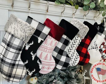 Puede incluir: Un conjunto de 8 calcetines de Navidad con varios patrones, incluyendo cuadros, renos y copos de nieve. Los calcetines están colgados en una chimenea blanca con un letrero que dice "Hecho a mano en los Estados Unidos".