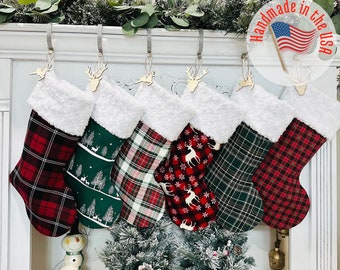 May include: Six Christmas stockings with a white faux fur cuff and various plaid patterns, including red and black, green and black, and red and white. The stockings are hung on a white mantel with a wooden reindeer ornament on each stocking.