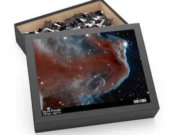 May include: An open puzzle box with a space-themed image on the lid. The image features a nebula with red, blue, and white colors. The box is gray and contains puzzle pieces. The box is labeled "8x10 Puzzle 120 pcs Ages 9+".