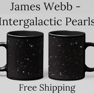 May include: Two black ceramic mugs with a celestial design featuring stars and galaxies. The mugs have a black handle and rim. The text "James Webb - Intergalactic Pearls" is printed above the mugs.