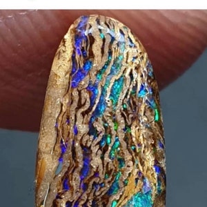 May include: A close-up of a blue, green, and gold opal gemstone. The opal has a unique pattern of swirling colors and a rough, natural texture.