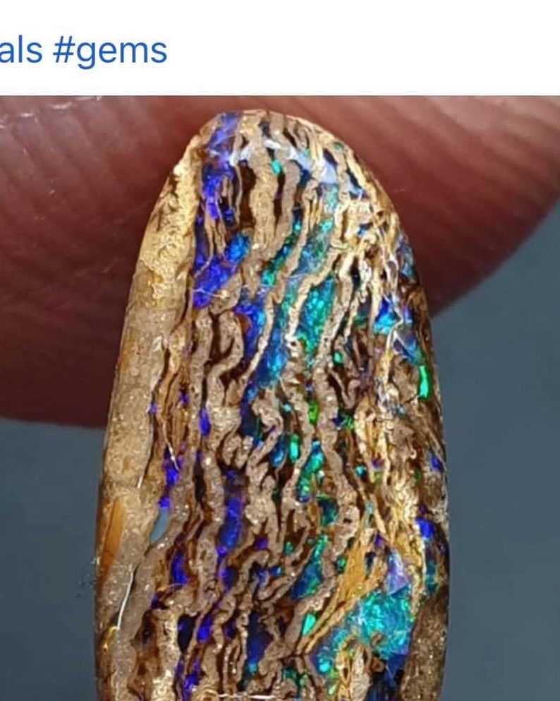 May include: A close-up of a blue, green, and gold opal gemstone. The opal has a unique pattern of swirling colors and a rough, natural texture.