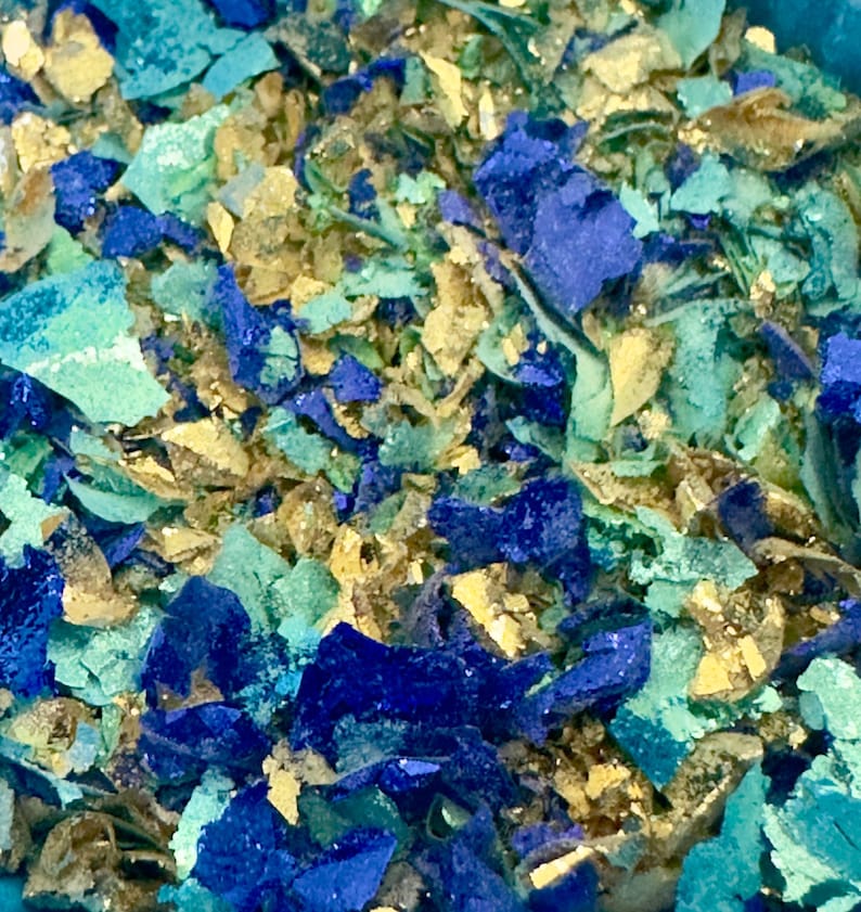 May include: A close-up of a mixture of blue, green, and gold glitter. The glitter is scattered randomly and appears to be made of small, irregular pieces.