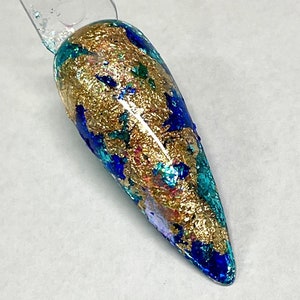May include: A close-up of a long, pointed, blue and gold nail with a metallic finish. The nail is decorated with gold flakes and has a teal and blue base.