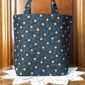 May include: A black tote bag with a pumpkin pattern. The bag has two handles and is made of fabric.
