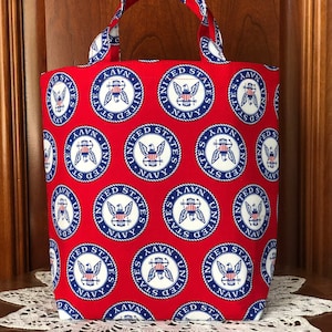 May include: Red tote bag with a white and blue United States Navy logo pattern. The bag has a single handle.