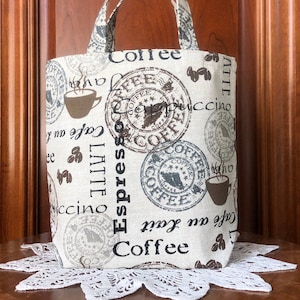 May include: A small, beige canvas tote bag with brown coffee-themed print. The bag has two handles and features the words "Coffee", "Espresso", "Latte", and "Cafe au Lait" printed on it.