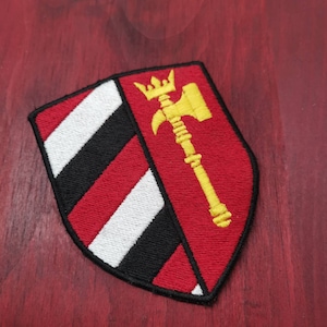 Könnte beinhalten: Ein rot-weiß-schwarz gestreiftes Schild mit einem goldenen Hammer und einer Krone auf rotem Hintergrund.