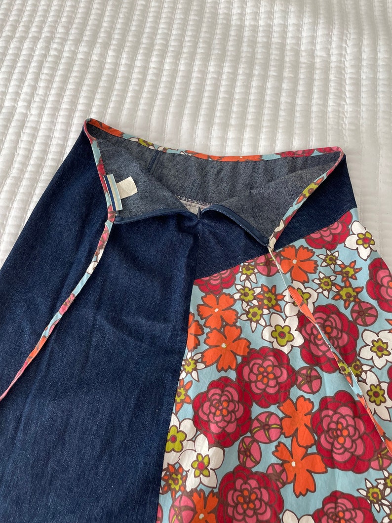 K&ouml;nnte beinhalten: Ein Jeansrock mit einem floralen Print-Panel. Der Rock hat einen Wickelstil und einen Bindeverschluss. Der florale Print ist in Rot-, Orange-, Rosa- und Gr&uuml;nt&ouml;nen auf einem hellblauen Hintergrund.