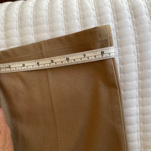 Op de afbeelding: Een close-up van de onderkant van een kaki broek met een meetlint dat een lengte van 8 inch aangeeft.