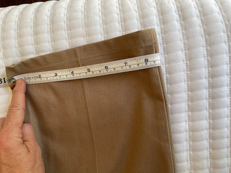 Op de afbeelding: Een close-up van de onderkant van een kaki broek met een meetlint dat een lengte van 8 inch aangeeft.