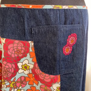 K&ouml;nnte beinhalten: Ein Jeansrock mit einem Stoffpanel mit Blumenmuster und einer Ges&auml;&szlig;tasche mit gestickten rosa Blumen.