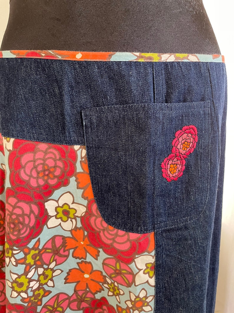 K&ouml;nnte beinhalten: Ein Jeansrock mit einem Stoffpanel mit Blumenmuster und einer Ges&auml;&szlig;tasche mit gestickten rosa Blumen.