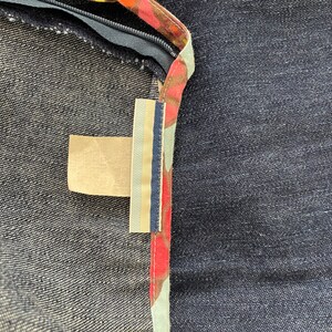 K&ouml;nnte beinhalten: Nahaufnahme eines Jeansstoffes mit einem braunen, roten und wei&szlig;en Musterbesatz. Ein kleines, rechteckiges, beigefarbenes Etikett ist am Besatz befestigt.