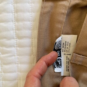 Op de afbeelding: Een beige canvas draagtas met een zwart-wit label waarop "Lime and Place" staat en wasinstructies. Het label bevat ook de volgende informatie: RN 40085, 50% katoen, 50% polyester, lot 98 55520, stijl C2485.