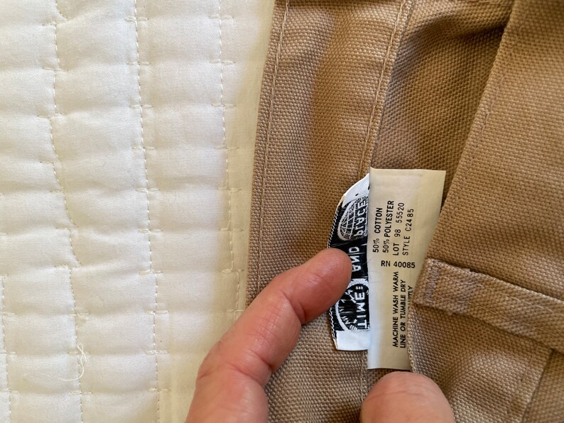 Op de afbeelding: Een beige canvas draagtas met een zwart-wit label waarop "Lime and Place" staat en wasinstructies. Het label bevat ook de volgende informatie: RN 40085, 50% katoen, 50% polyester, lot 98 55520, stijl C2485.