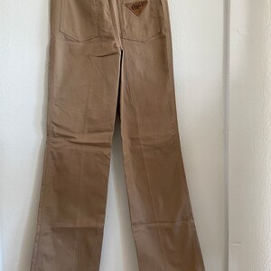 Op de afbeelding: Een beige, rechte broek met een bruin leren patch op de achterzak met de tekst "Candids".