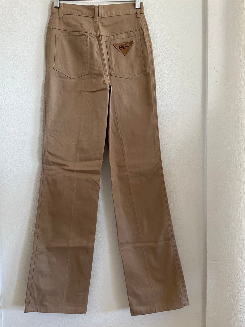 Op de afbeelding: Een beige, rechte broek met een bruin leren patch op de achterzak met de tekst "Candids".